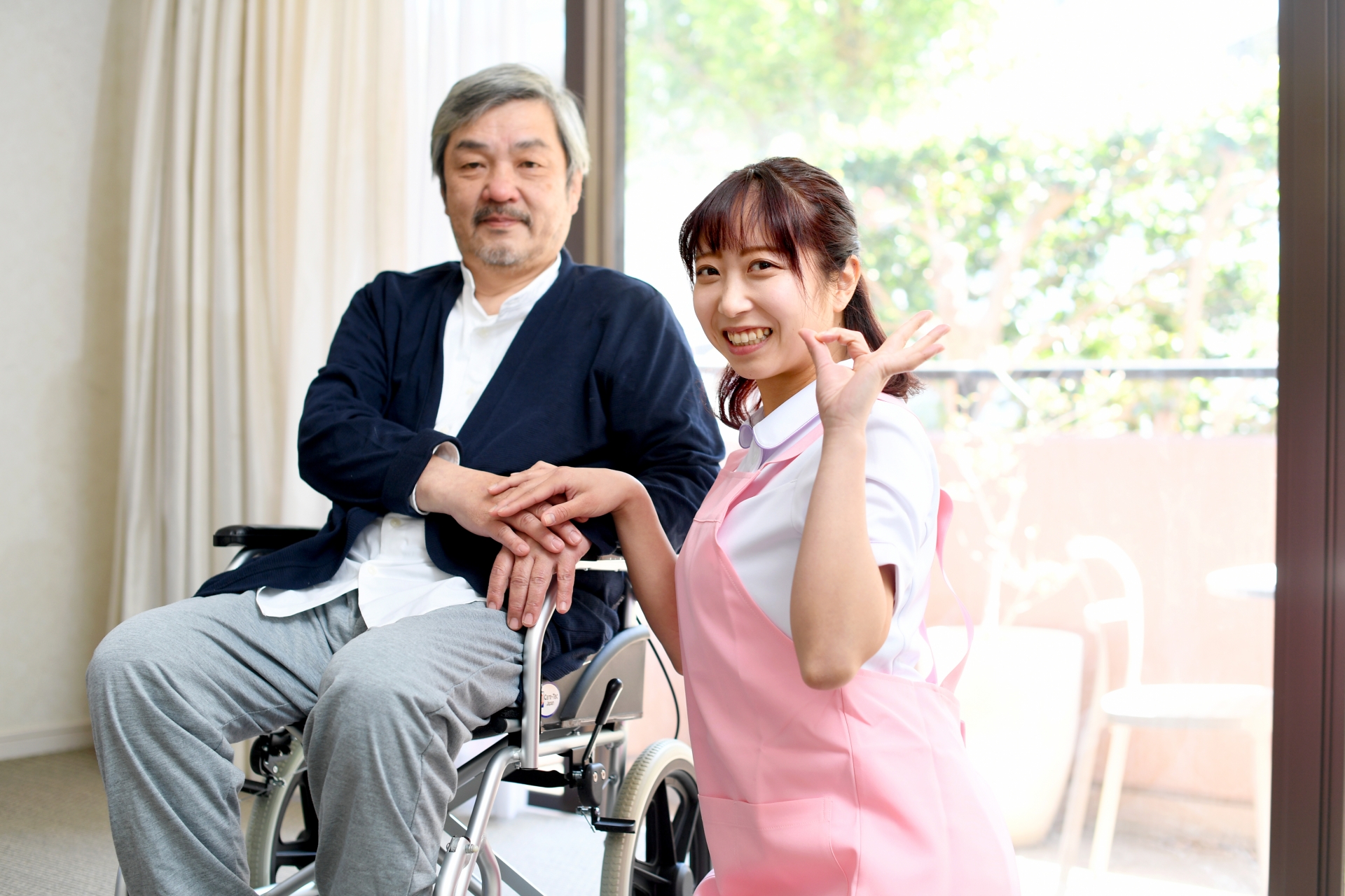 車椅子の利用者男性とOKサインをする女性介護スタッフ